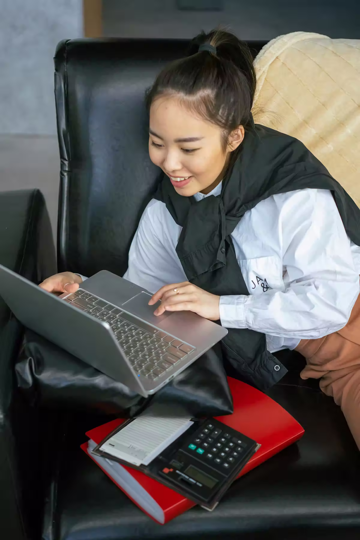 Girl looking at laptop with calculator beside her so she can calculate her QNET earnings