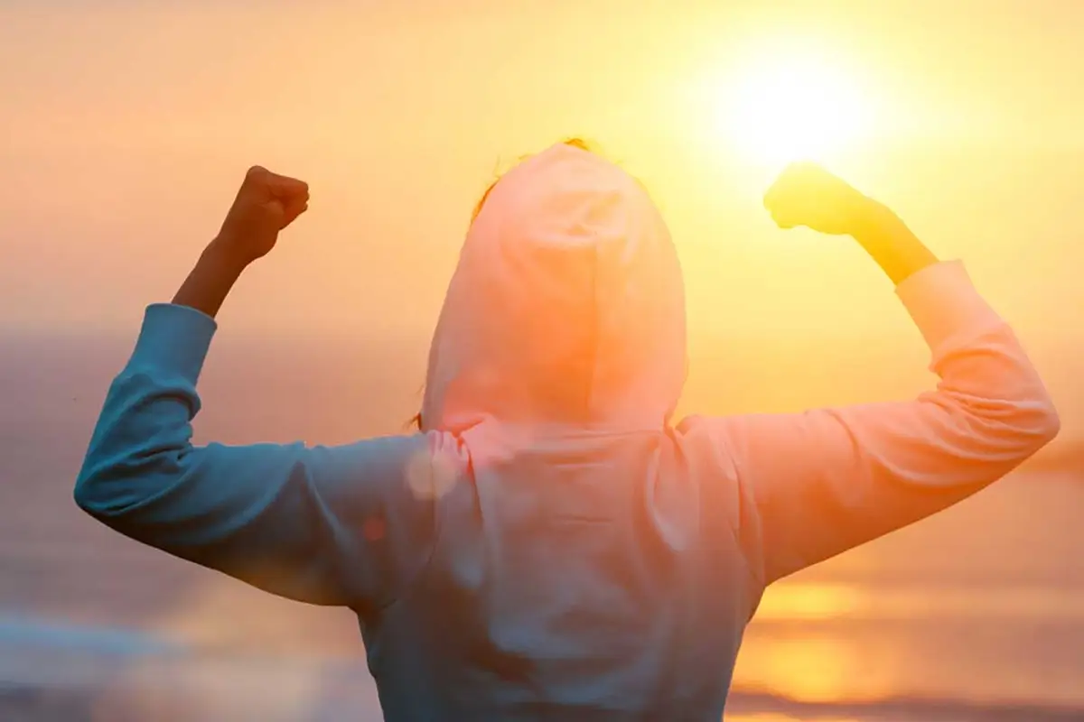 woman flexing arms while facing the sunset 